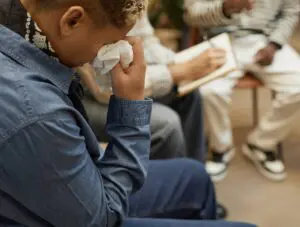 A man cries while another takes notes during a meeting in preparation for a funeral for a stranger.