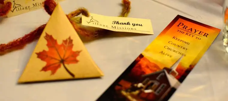 Items from a banquet supporting rural church ministry in Canada are laid out on a table: a bookmark, a prayer favor, and a thank you note.